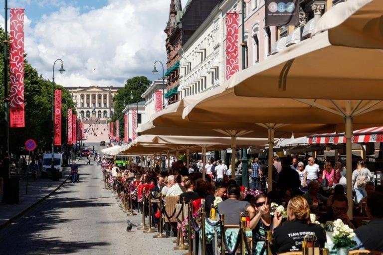 un grupo de personas sentadas en mesas bajo sombrillas en una calle en City Pulse, en Oslo