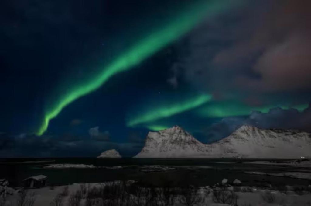 an aurora in the sky over a snowy mountain at Explorers Cabin Lofoten in Offersøya