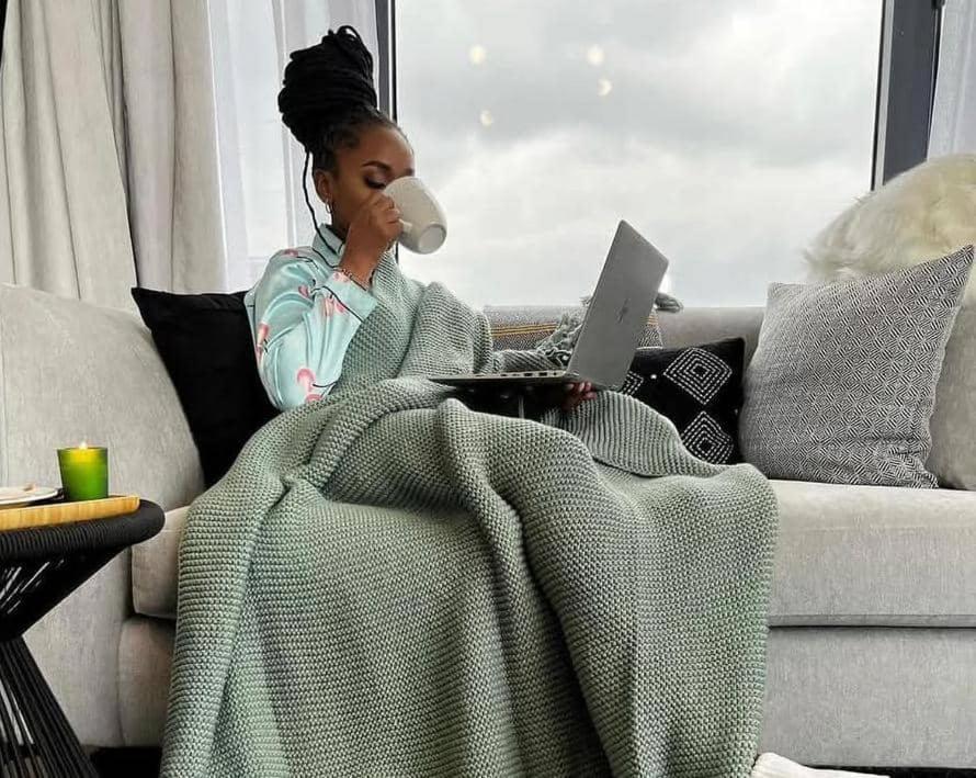 Kampala Apartments في كامبالا: امرأة تجلس على الأريكة مع كوب من القهوة وجهاز كمبيوتر محمول