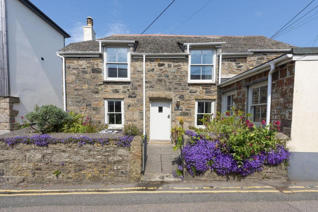 een stenen huis met een witte deur en paarse bloemen bij Piskey Cottage, Mousehole - Close to Harbourside - Free WiFi - Free Parking in Mousehole