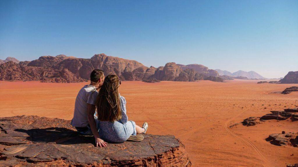 a man and woman sitting on a rock in the desert at Wadi Rum Spring Moon & Jeep Tour in Wadi Rum