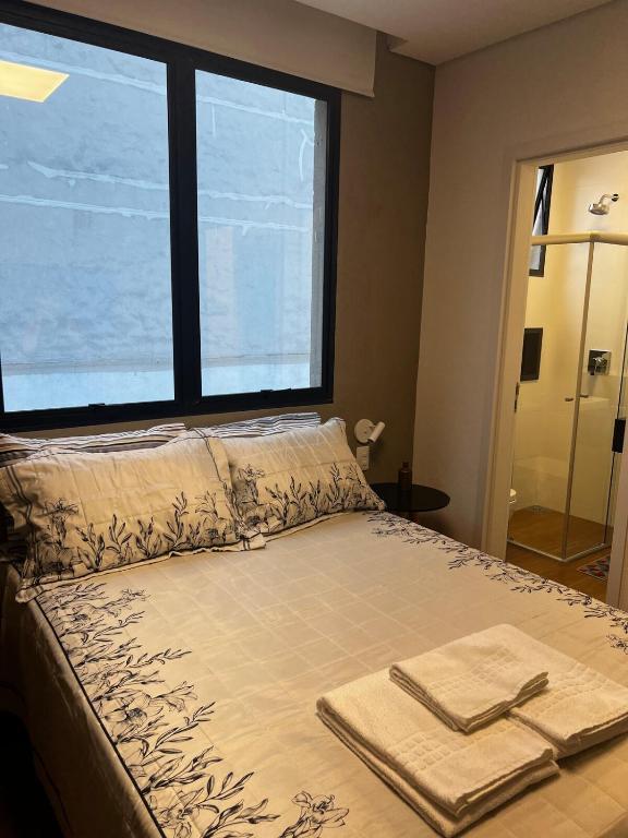 a bed with two towels on it with a large window at Guaja 745 - Apartamento Luca in Belo Horizonte
