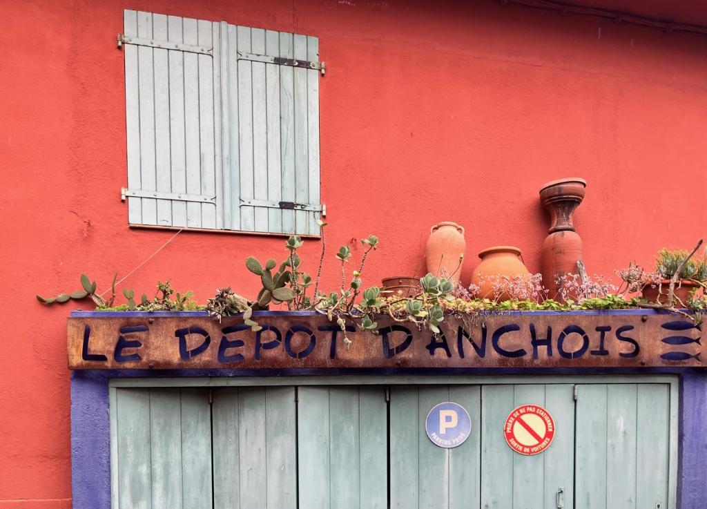un panneau sur un bâtiment avec des pots et des plantes dessus dans l'établissement The Depot Anchois, à Collioure