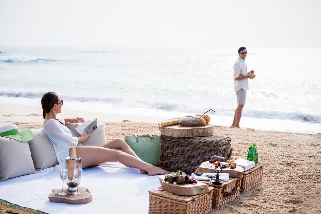 a woman sitting on a beach with a book and a man standing on the beach at Anantara Peace Haven Tangalle Resort in Tangalle