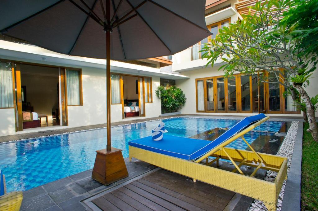 a pool with an umbrella and a blue recliner next to a house at Villa Travis in Seminyak