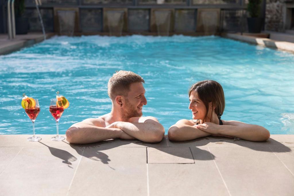 a man and woman laying in a swimming pool with wine glasses at Hotel Delle Terme Santa Agnese in Bagno di Romagna