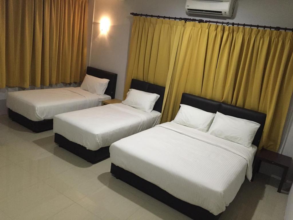 two beds in a hotel room with yellow curtains at JS&K Homestay in Kuala Terengganu