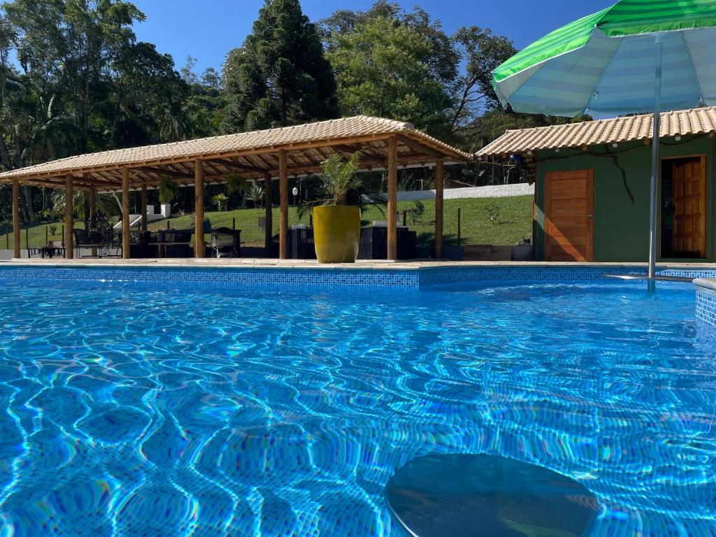 a swimming pool with an umbrella and a house at Sitio Renovo Juquitiba Hospedagens in Juquitiba