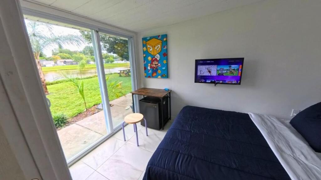 Un dormitorio con una cama y un televisor y una ventana. en Small Lakeview Suite Near Disney & Universal, en Kissimmee