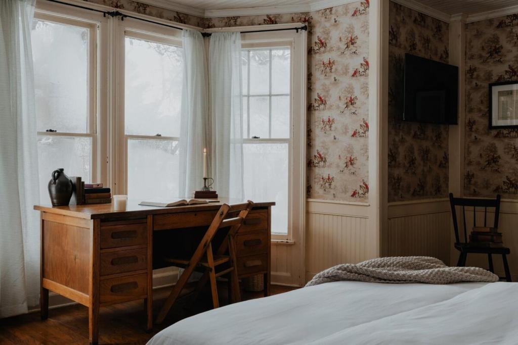 Schlafzimmer mit einem Schreibtisch, einem Bett und Fenstern in der Unterkunft Book Village Inn - Twain Room Queen Bed in Hobart