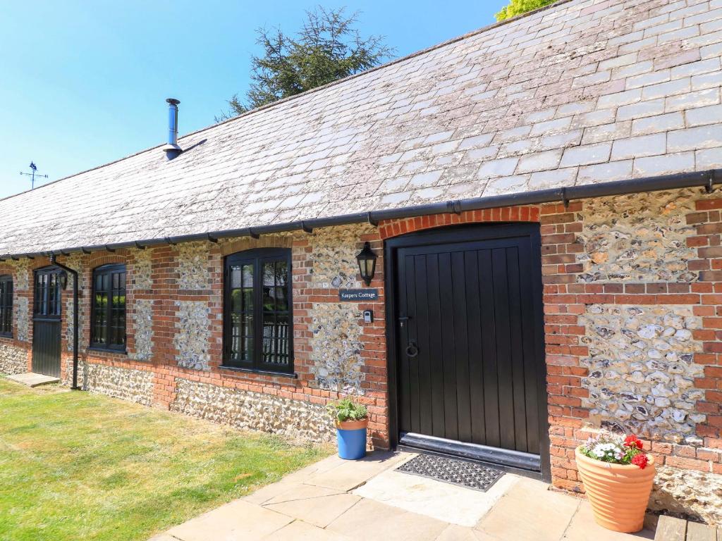 ein altes Backsteingebäude mit einer schwarzen Tür in der Unterkunft Keepers Cottage in Blandford Forum