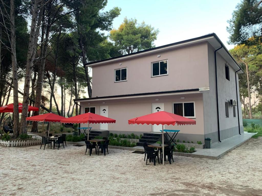un edificio con mesas, sillas y sombrillas rojas en Vila Topi, en Vlorë
