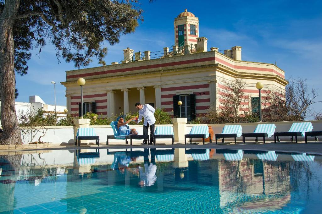 un homme debout à côté d'une piscine en face d'un bâtiment dans l'établissement Villa La Meridiana - Caroli Hotels, à Leuca