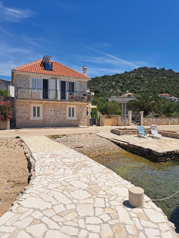a house with a stone walkway next to a body of water at Insel Kaprije Nowak in Kaprije