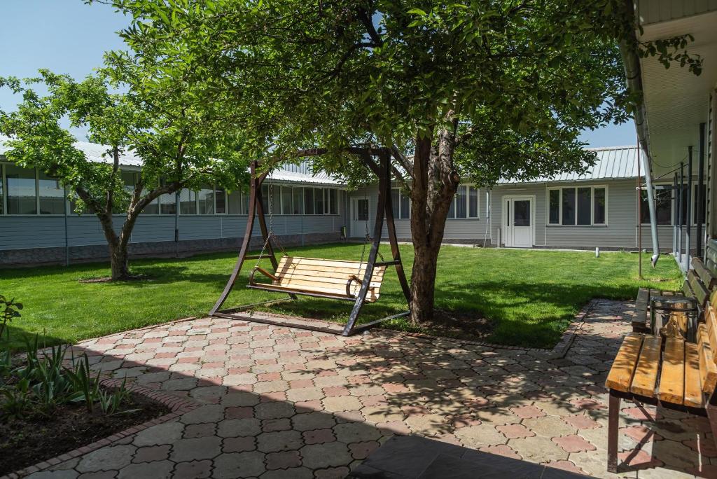 eine Parkbank unter einem Baum in einem Hof in der Unterkunft Sunny Valley Guest House Karakol in Karakol