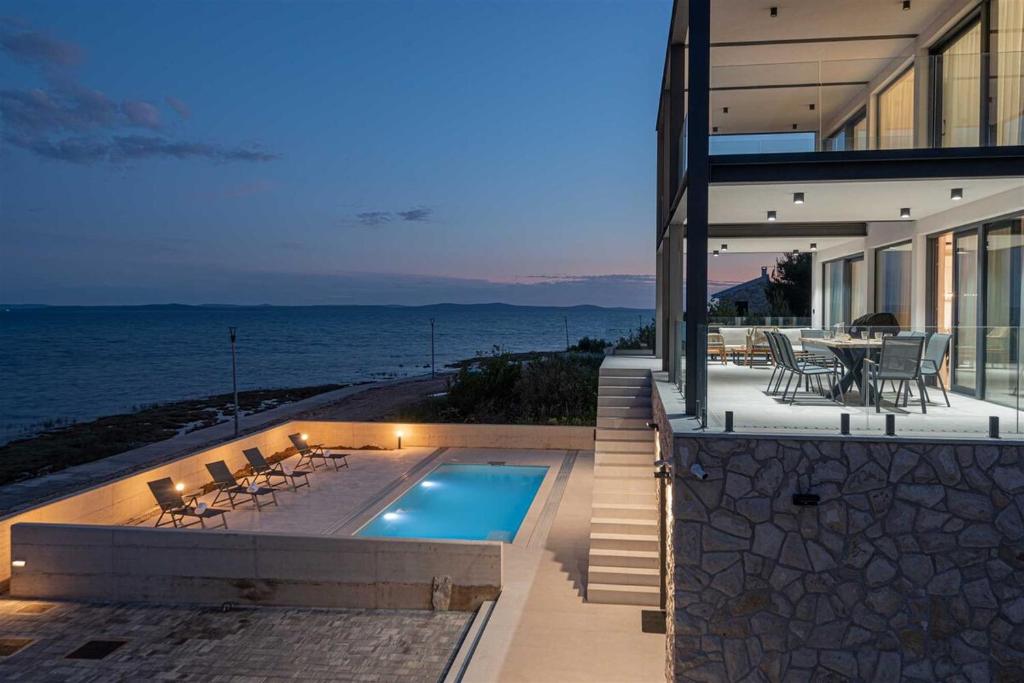 a house with a swimming pool next to the ocean at Villa Serena Luxury Seafront Escape with Pool in Privlaka