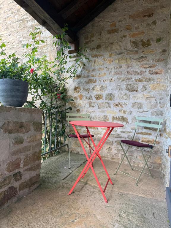 a red table and two chairs next to a brick wall at Chambre La Dracysienne in Dracy-le-Fort