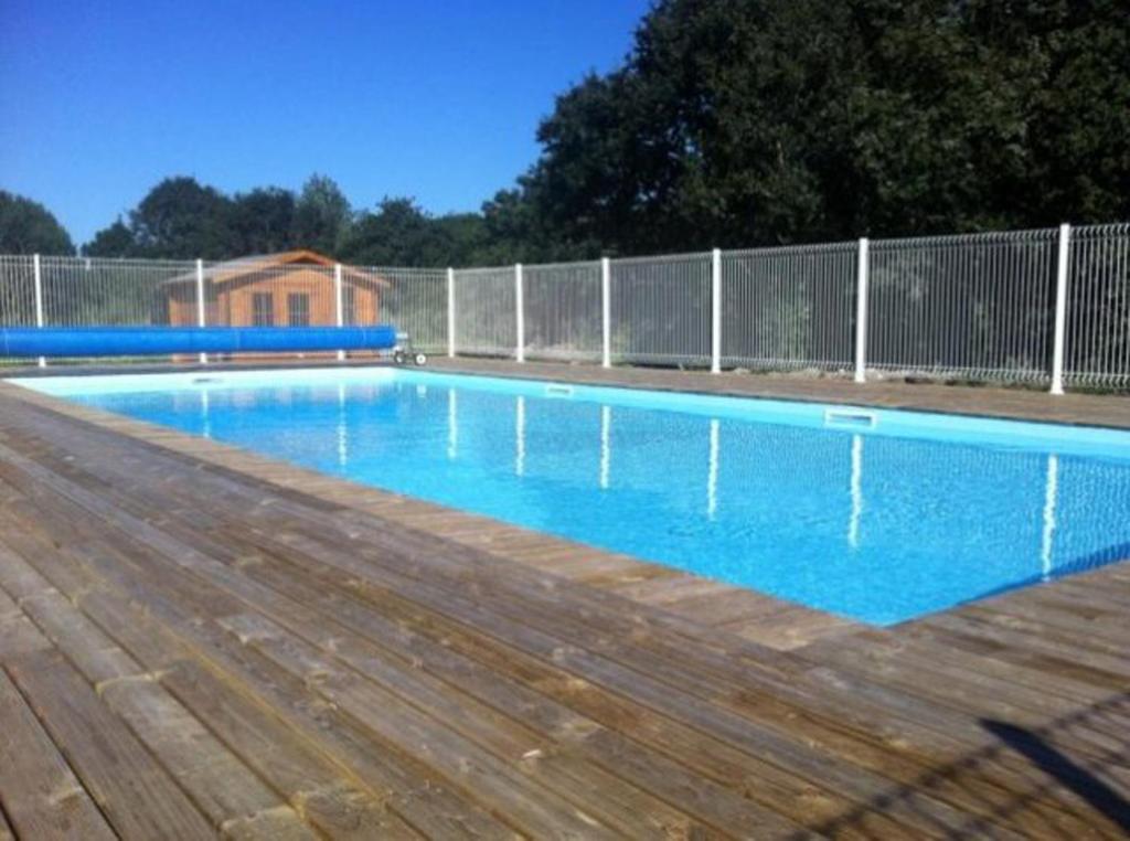 a blue swimming pool with a wooden deck and a fence at CHALET Les ALGUES in Plobannalec-Lesconil