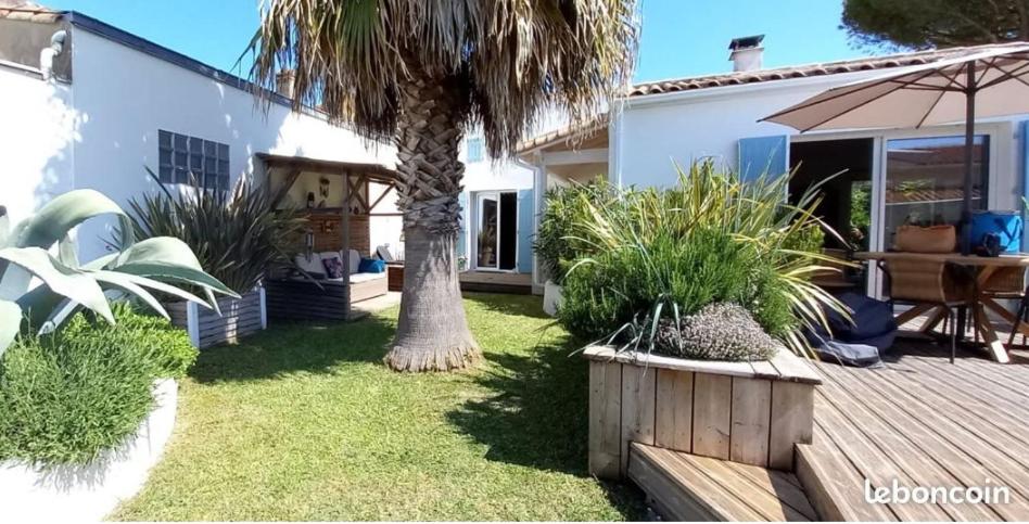 une cour arrière avec un palmier et une terrasse en bois dans l'établissement Charmante maison au calme proche des commodités, à Meschers-sur-Gironde