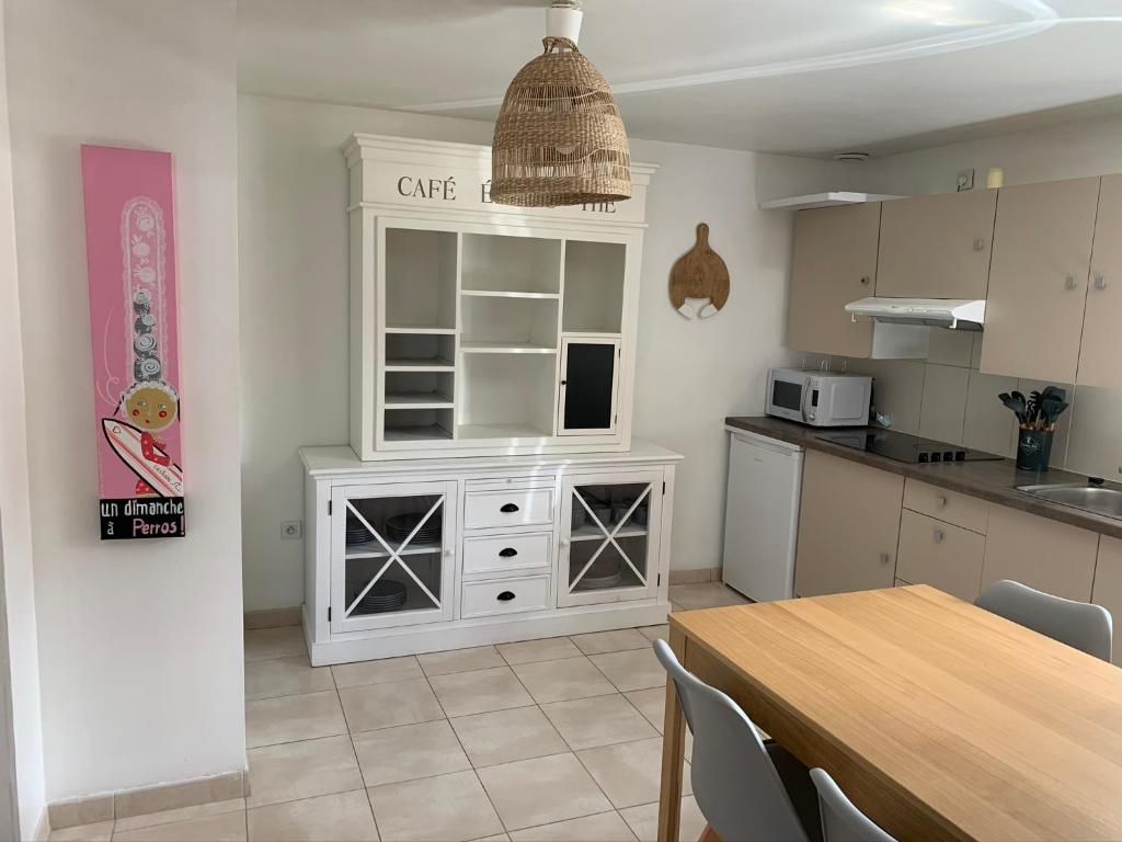 - une cuisine avec une table et une armoire blanche dans l'établissement Les Petites Maisons de la Clarté - La Bernique, à Perros-Guirec