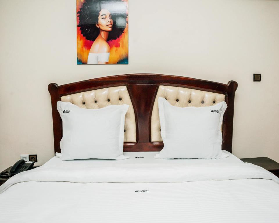 a bed with white pillows and a painting on the wall at Regal Hotel Douala in Douala