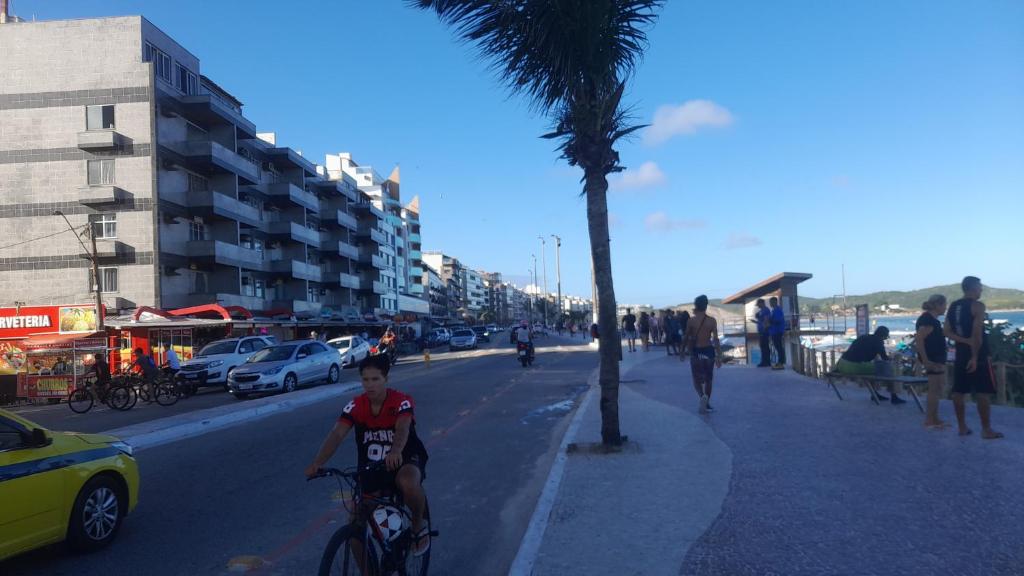 卡波布里奥Lindo apartamento de frente a praia do forte cabo frio的一个男孩骑着自行车沿着棕榈树旁的街道行驶