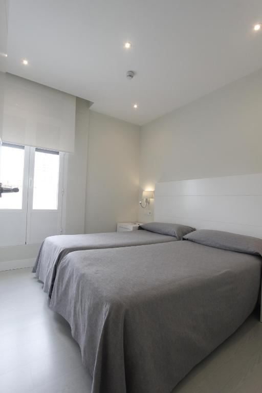 a white bedroom with two beds and a window at Rincón de Gran Vía in Madrid