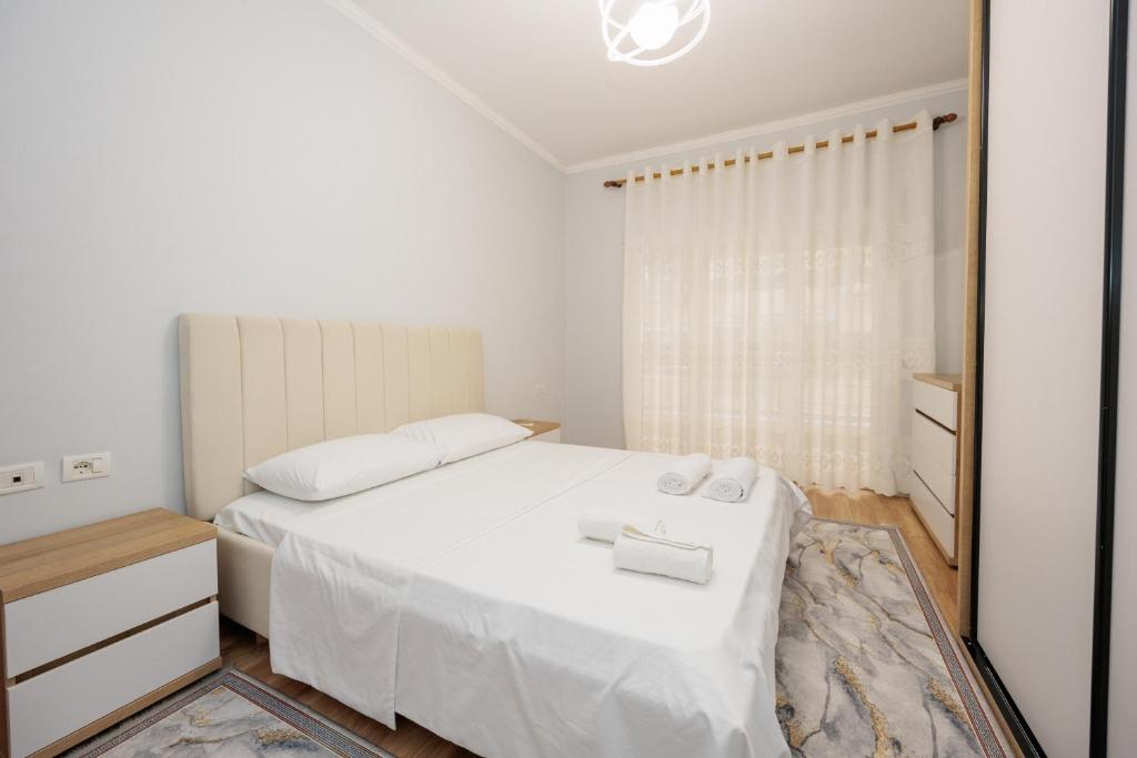 a white bedroom with a white bed and a mirror at IZZY Apartments in Tirana