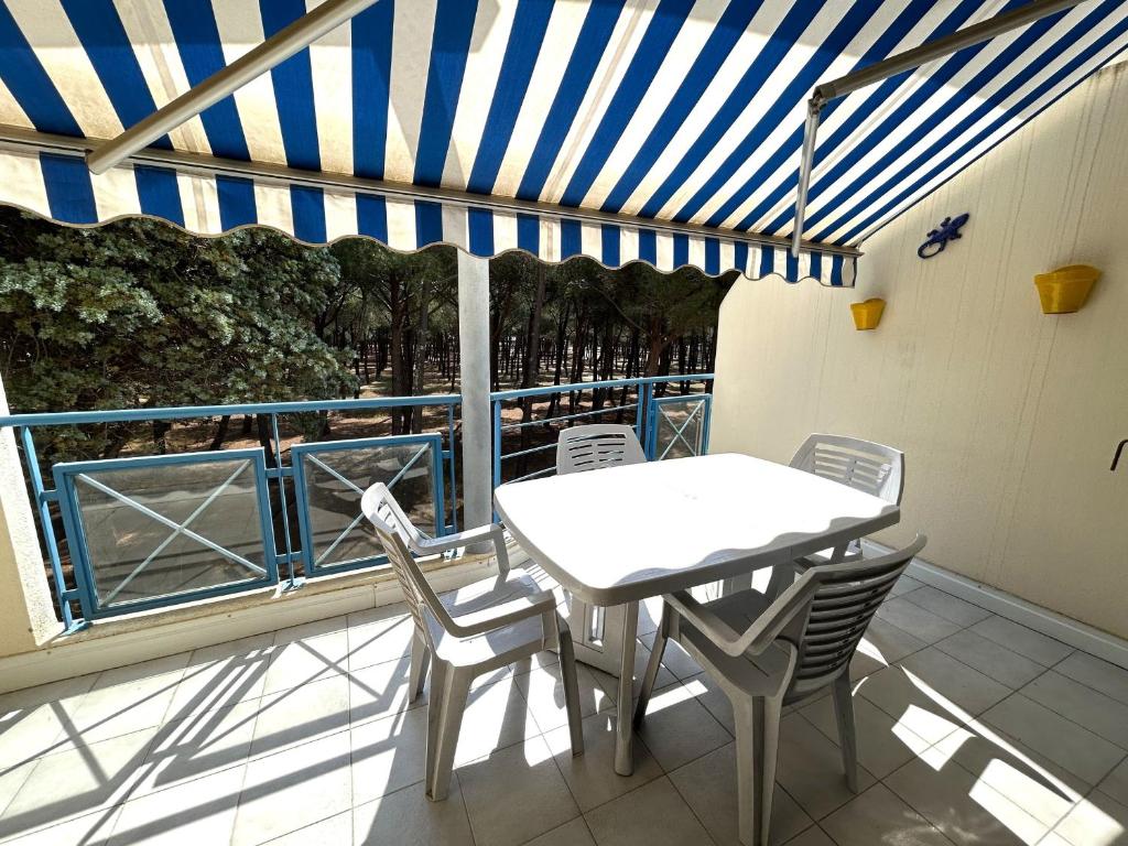 une table et des chaises sur un balcon avec un auvent bleu et blanc dans l'établissement Appartement 4/5 pers. face à la pinède avec terrasse - FR-1-837-13, à Argelès-sur-Mer