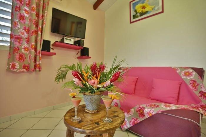een woonkamer met een roze bank en een tafel met bloemen bij Gîte Hibiscus piscine partagée in Saint-François