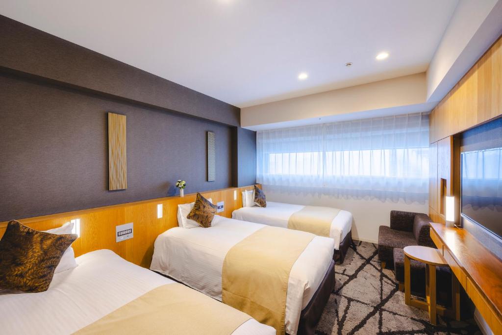 a hotel room with three beds and a desk at Hotel Gracery Shinjuku in Tokyo