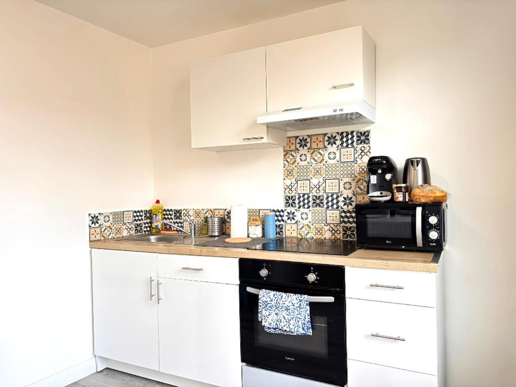 une cuisine avec des armoires blanches et un four noir dans l'établissement Urban Chic Studio 10 min de la gare, à Roanne