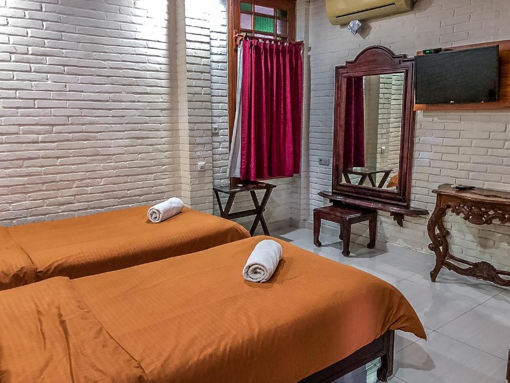 a room with two beds and a mirror and a tv at Arys Garden Hotel Yogyakarta in Yogyakarta
