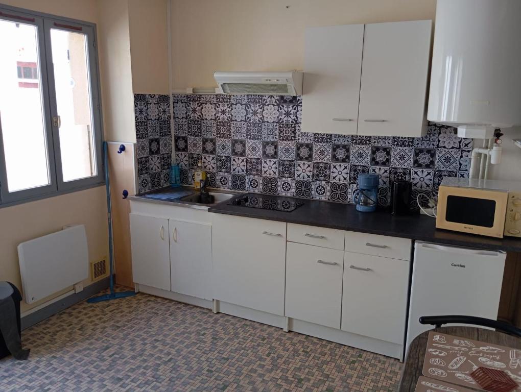 une cuisine avec des armoires blanches et un micro-ondes dans l'établissement Studio IRIS type T1, à Évaux-les-Bains