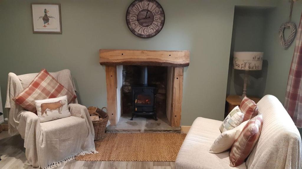 a living room with a fireplace and two chairs and a clock at A Cozy Bothy Retreat with Hot Tub in Keilour