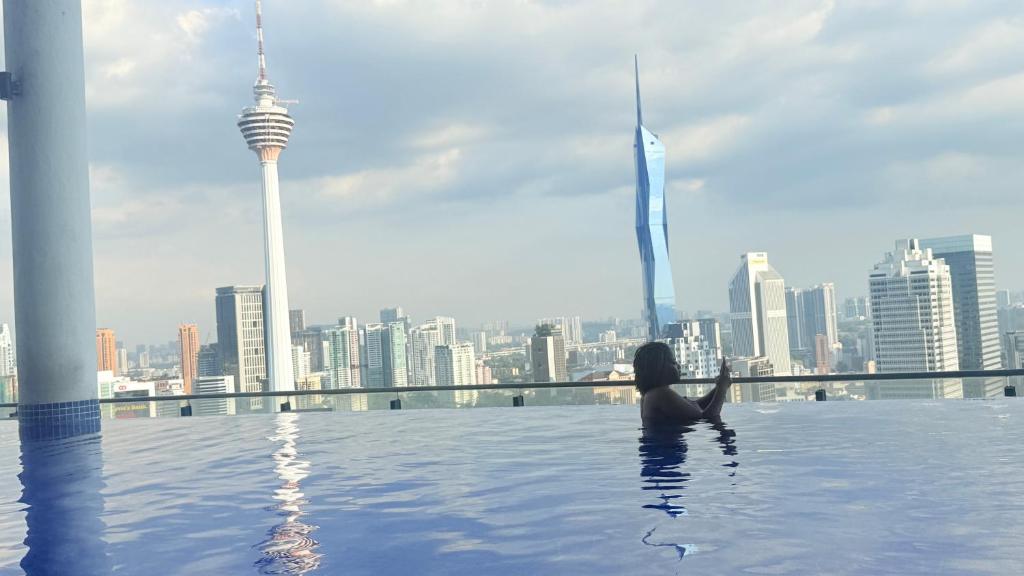 a woman sitting in a swimming pool with a view of a city at Colony Service Suites Kuala Lumpur in Kuala Lumpur