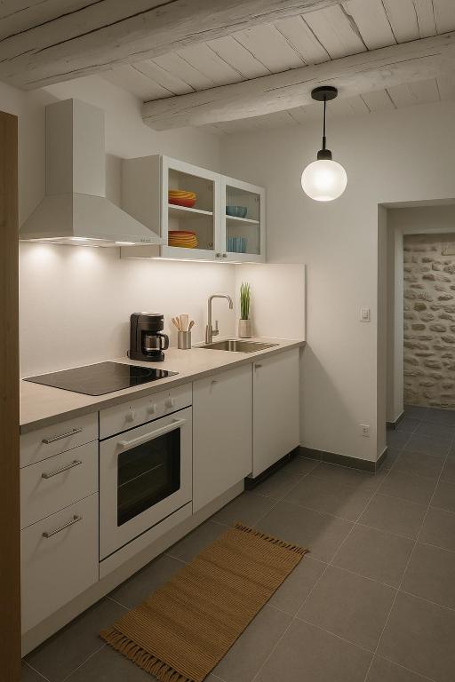 une cuisine avec des armoires blanches et un four à plaques de cuisson dans l'établissement Maison de village hyper centre, à LʼIsle-sur-la-Sorgue