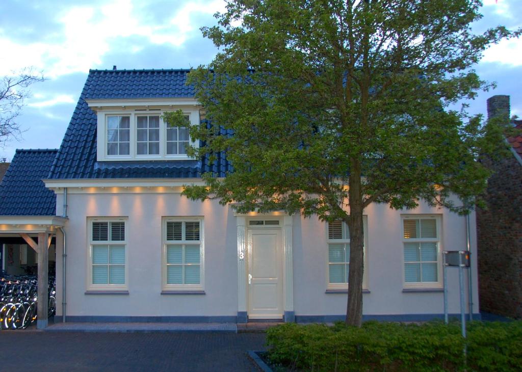 Una casa blanca con un árbol delante. en Kerkplein Vakanties, en Vrouwenpolder