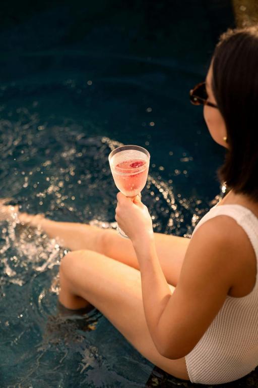 A guest sits in the water holding a pink drink.
