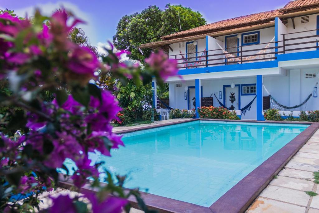 a swimming pool in front of a house with purple flowers at Pousada Pedra D'Água Pipa in Pipa