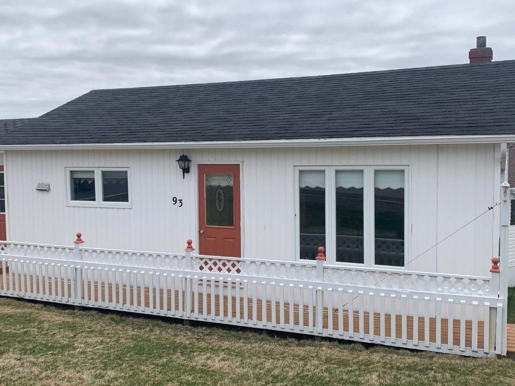 a white house with a red door and a fence at Long Beach Lookout Vacation Rental in Twillingate