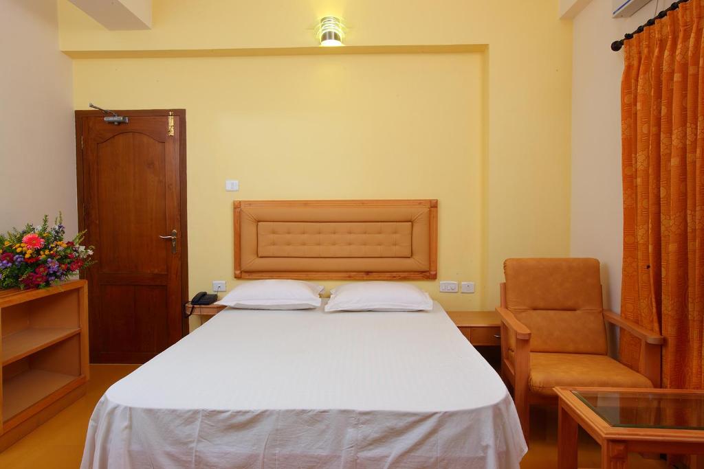 a bedroom with a white bed and a chair at Rajavalsam Guruvayur in Guruvāyūr