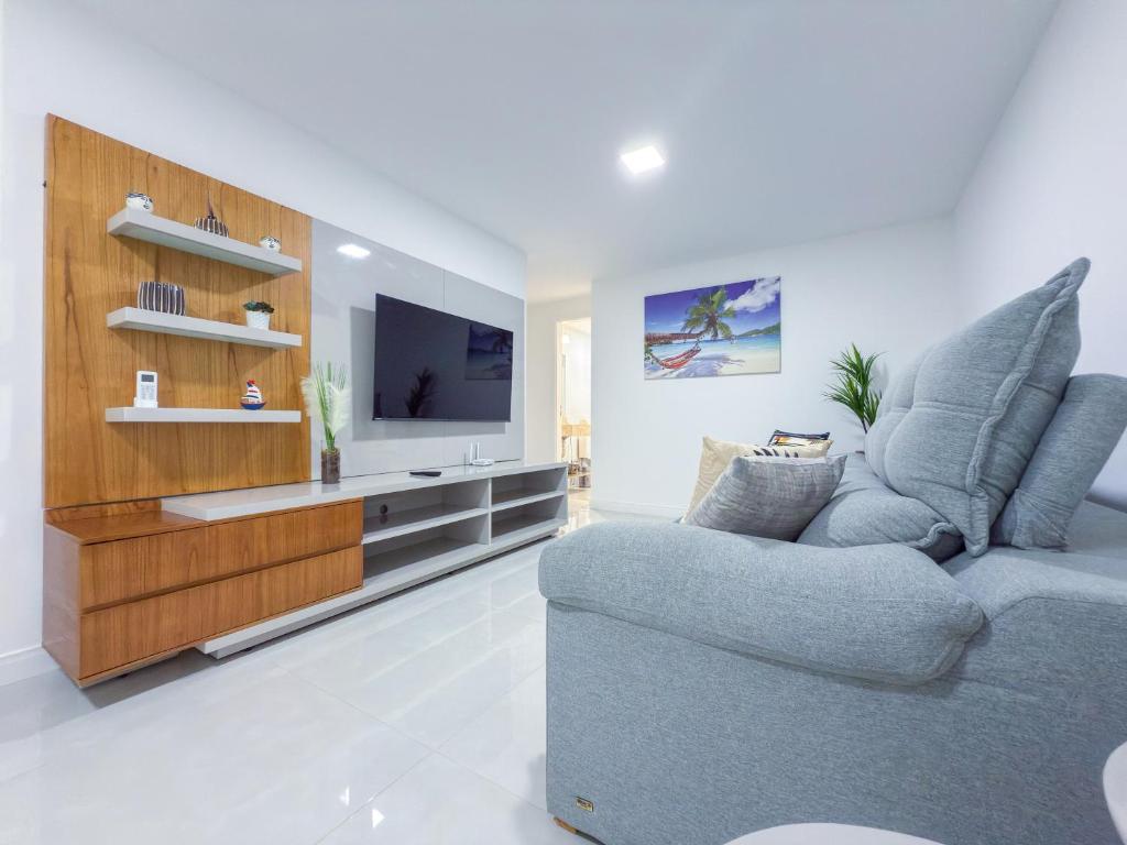 a living room with a blue couch and a television at Apartamento Vista Mar a 50m da Praia dos Anjos com Piscina, Churrasqueira Privativa e Estrutura de Lazer Completa in Arraial do Cabo