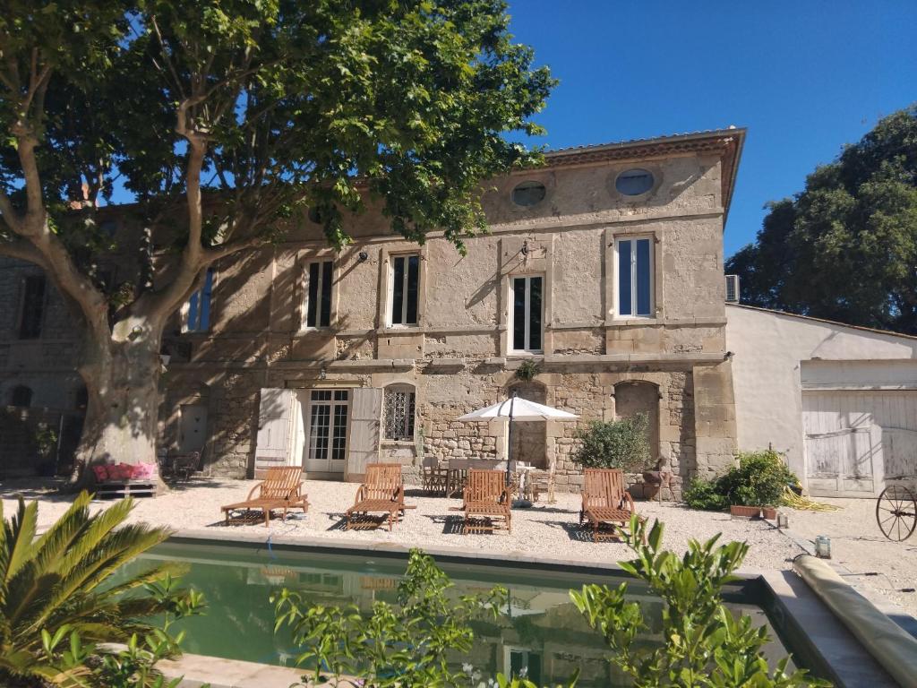 - un bâtiment avec une piscine, des chaises et un parasol dans l'établissement Cœur de Mas entre Alpilles et Camargue avec piscine et climatisation - 2 chambres, à Arles