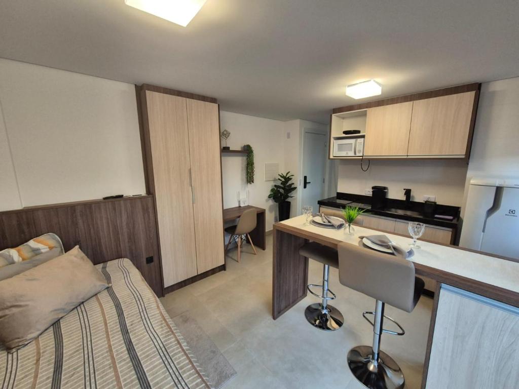 a living room with a kitchen and a room with a bed at Studio Novo e completo perto da PUC in Curitiba