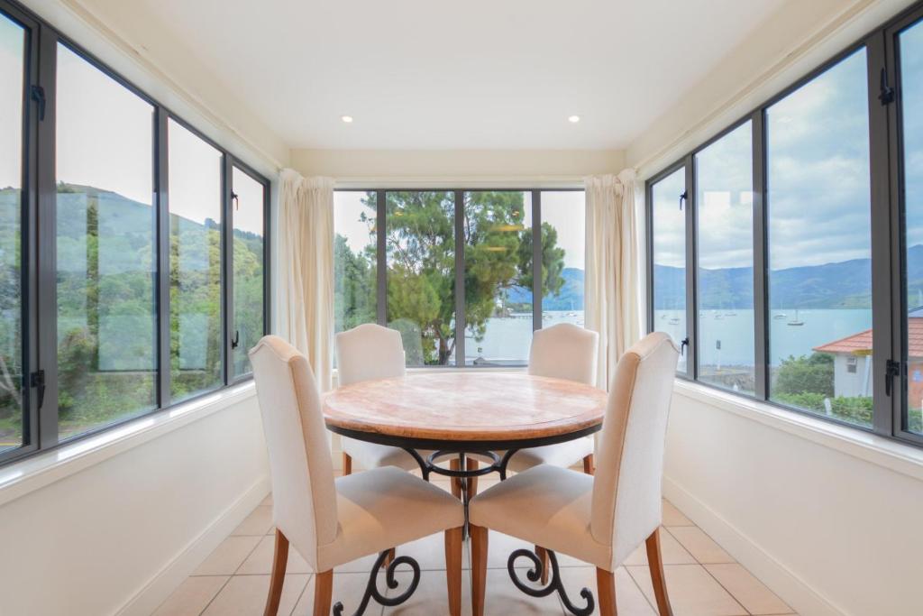 a dining room with a table and chairs and large windows at Waterfront Akaroa Retreat with Harbour Views & Balcony in Akaroa