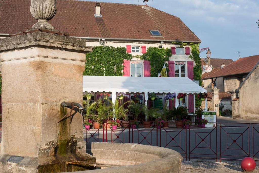 a fountain in front of a pink house with a white canopy at Logis Auberge de la Fontaine in Villiers-sur-Suize