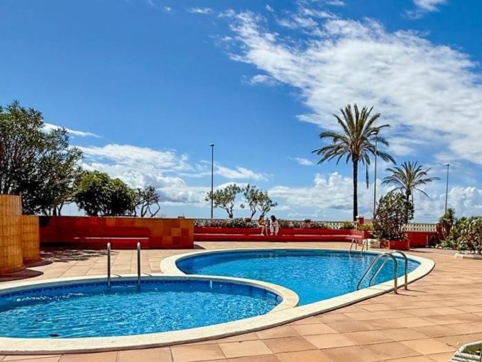 a swimming pool in a courtyard with palm trees at Winahost Apartamentro Cunit Vistas al Mar in Cunit