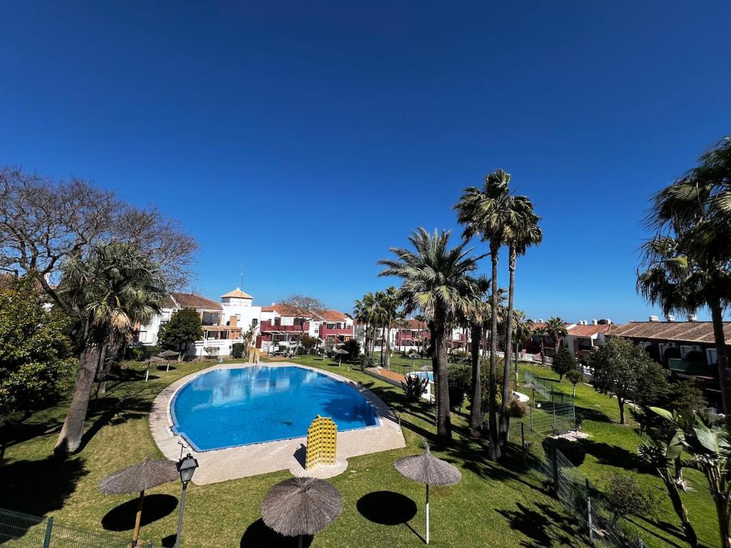 a swimming pool with palm trees and umbrellas at Apartamento Riviera in Novo Sancti Petri
