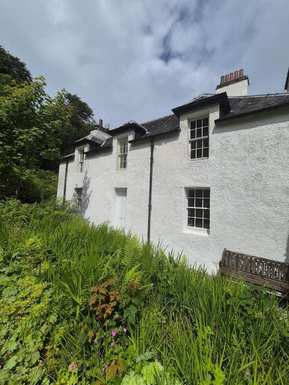 a white building on a hill with grass and flowers at Mackinnon Cottage - 3 bedroom Cottage in Broadford